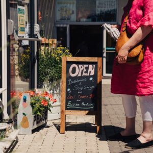 Woman standing in front of one of the shipping container shops, there's an A frame chalk board with 'Open' written on it.