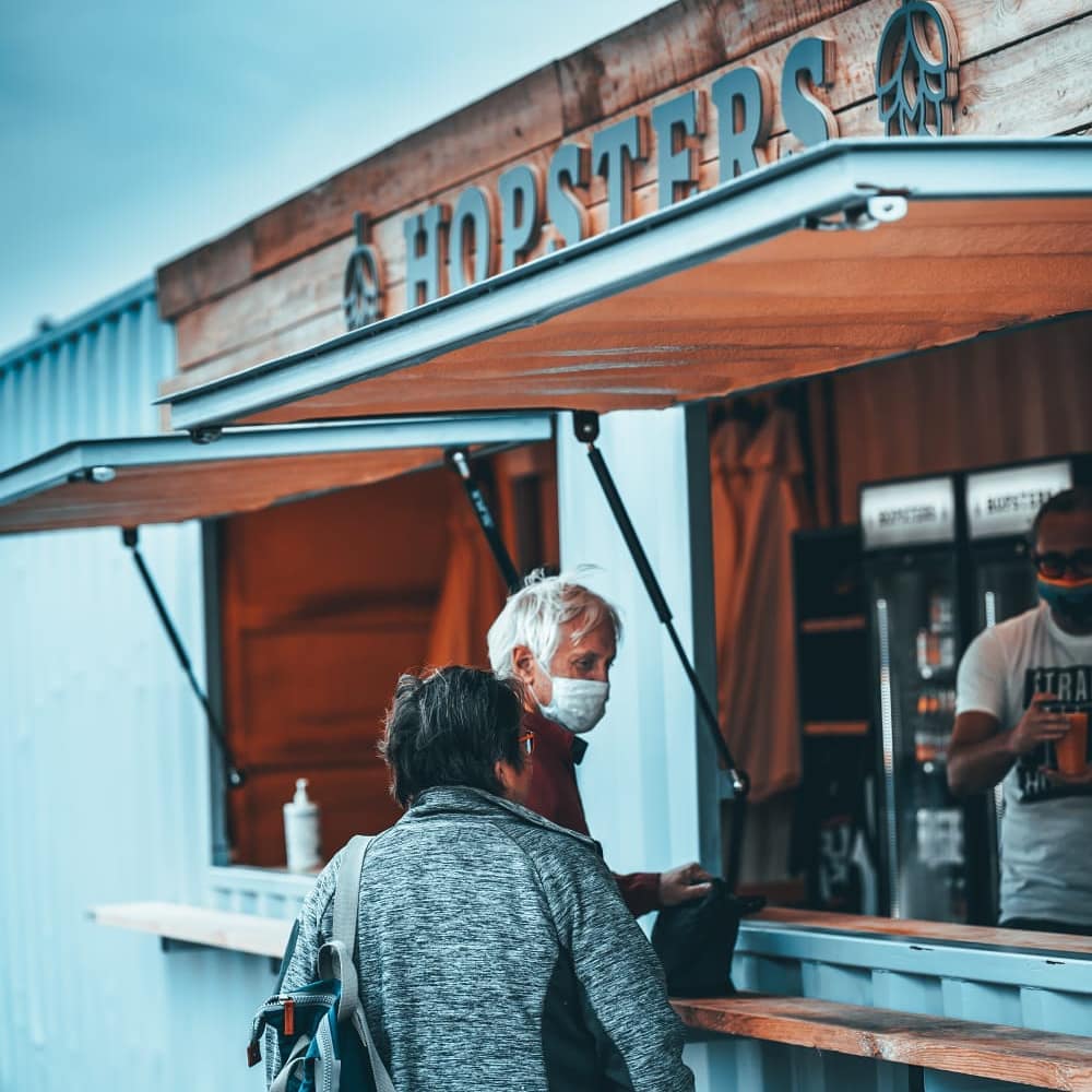 A couple order drinks at the Hopsters bar, housed in a light blue container.