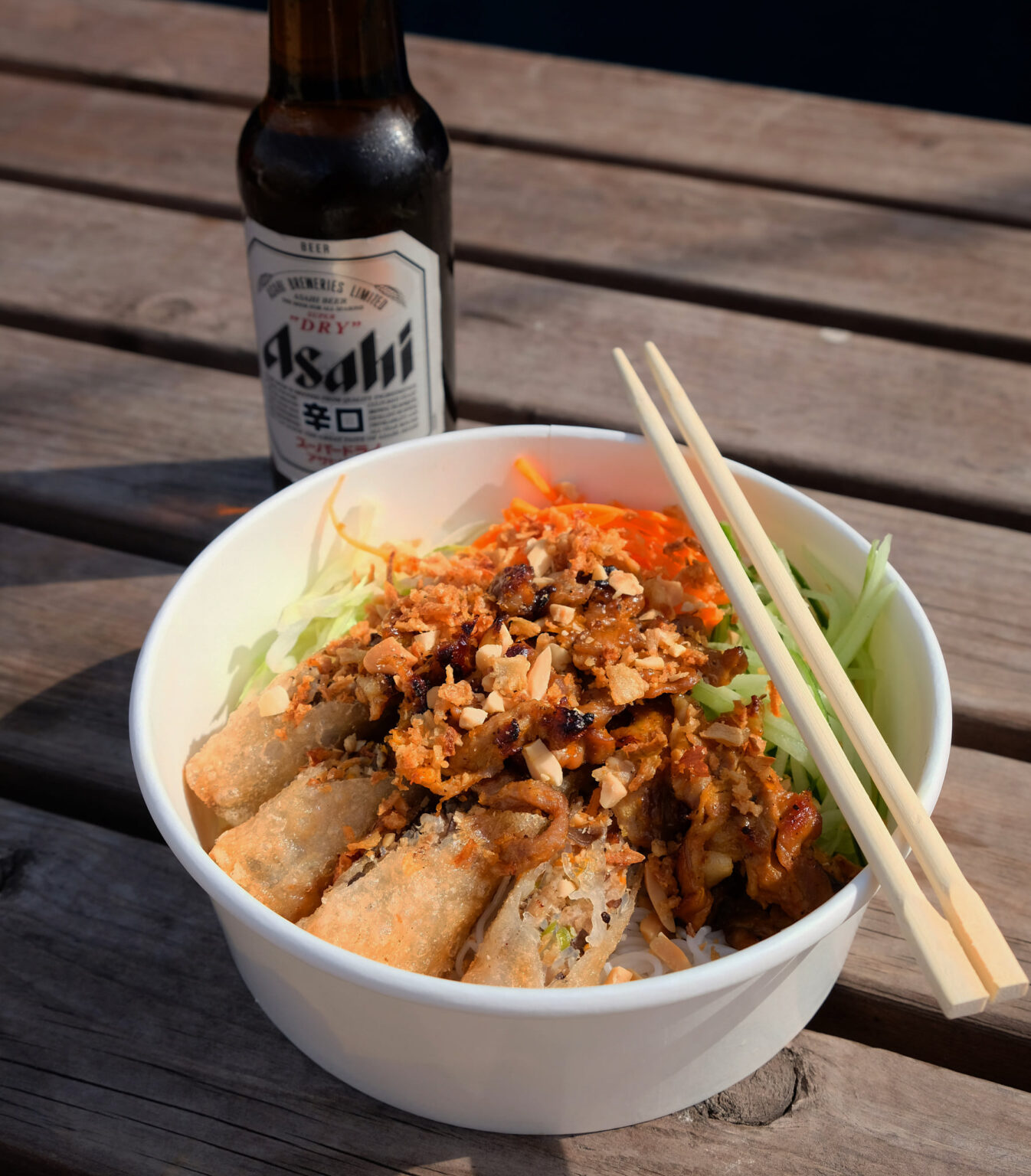 Bowl of Vietnamese food with chopsticks and bottle of beer.