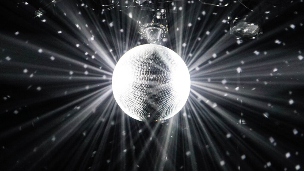 Black and white image of a glitter ball, reflecting light into the darkness. 